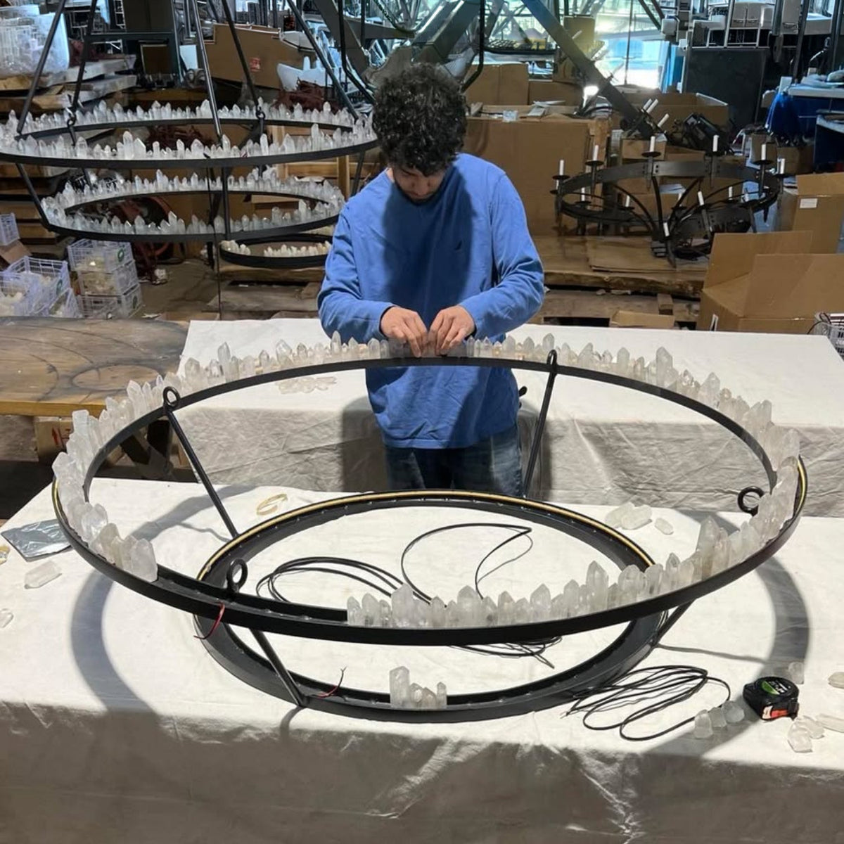 Ashore Lighting artisan fabricating a wrought iron chandelier, showing the handcrafted metalwork behind the finished lighting fixture.