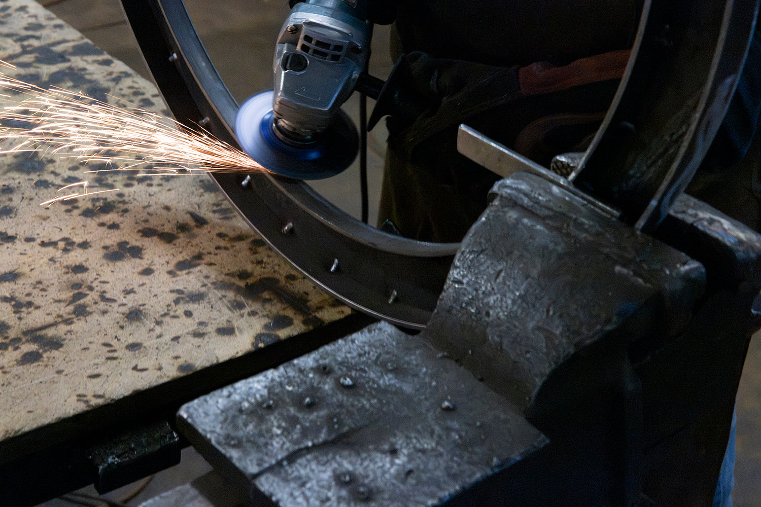 Ashore Lighting artisan grinding a large circular iron frame during wrought iron chandelier fabrication in the workshop