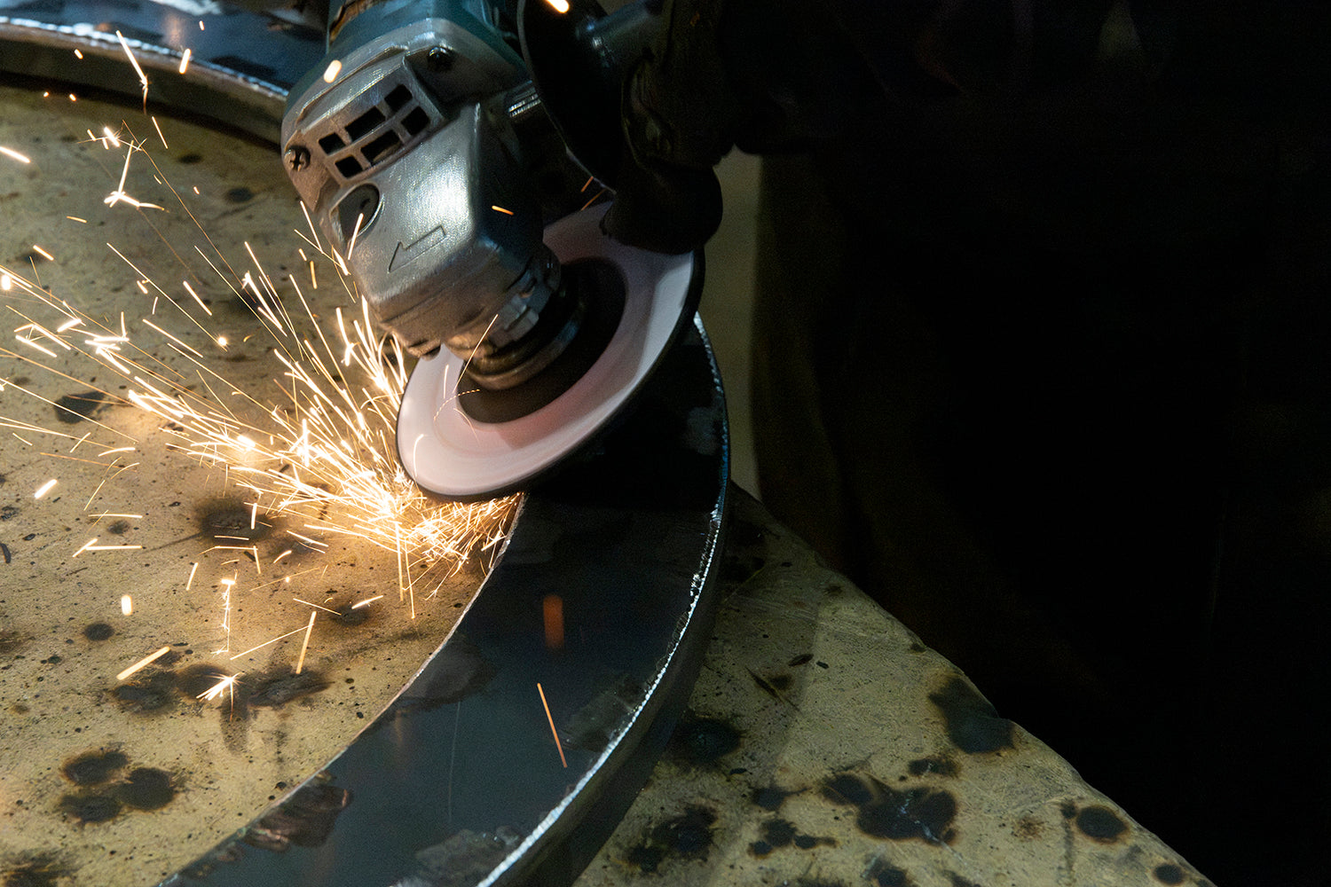 Ashore Lighting ironworker grinding a circular wrought iron component by hand in the lighting workshop.