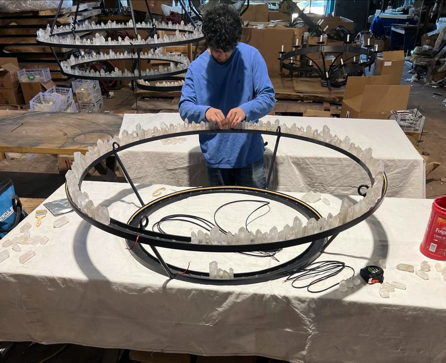 Craftsman assembling clear natural crystal points along the iron frame of a custom chandelier in the Ashore Lighting workshop.