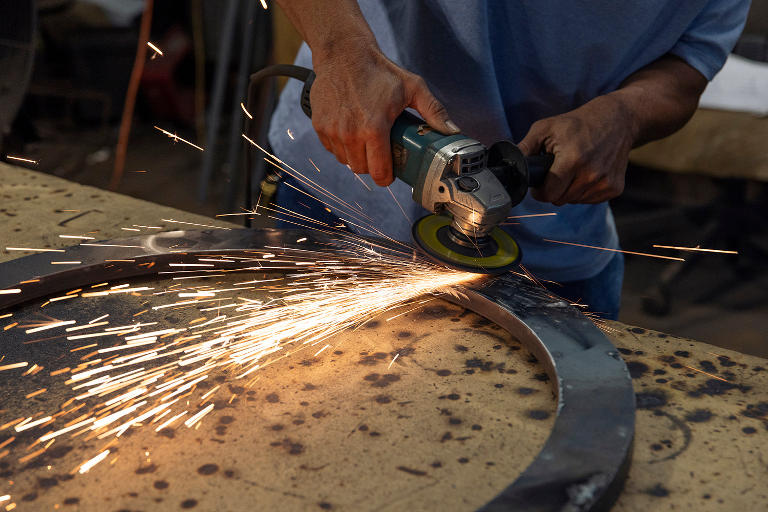 Ironworker grinding a circular iron chandelier frame in the workshop as part of the fixture fabrication and refinement process.