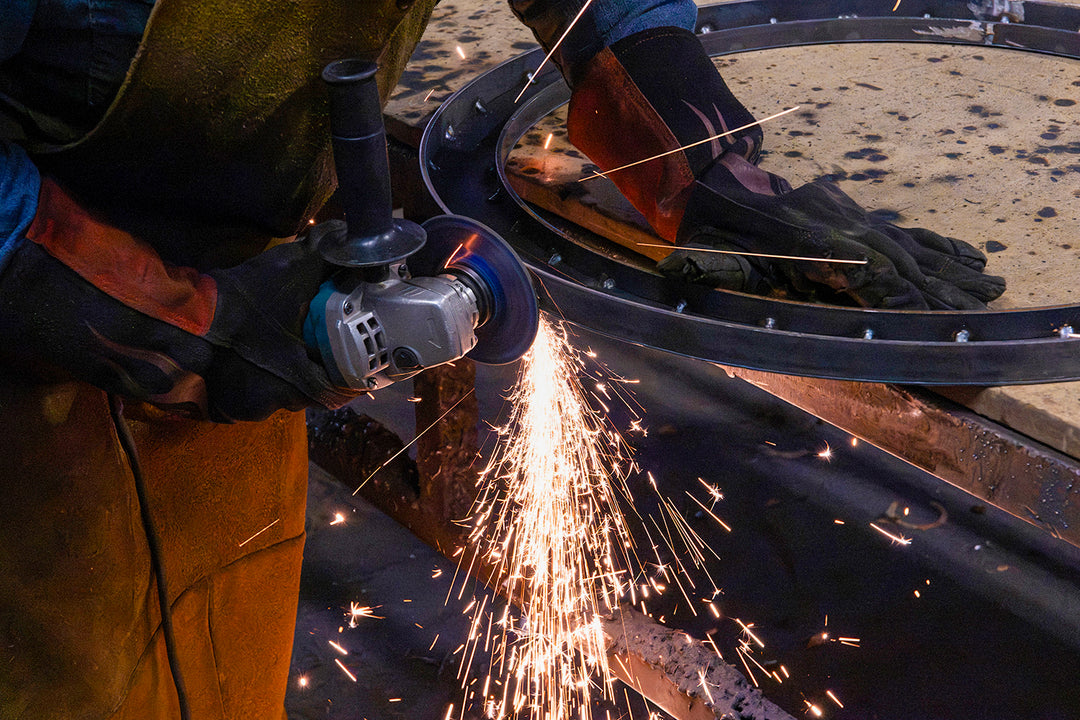 Artisan grinding and refining a circular iron lighting frame by hand before the fixture receives its selected decorative finish.