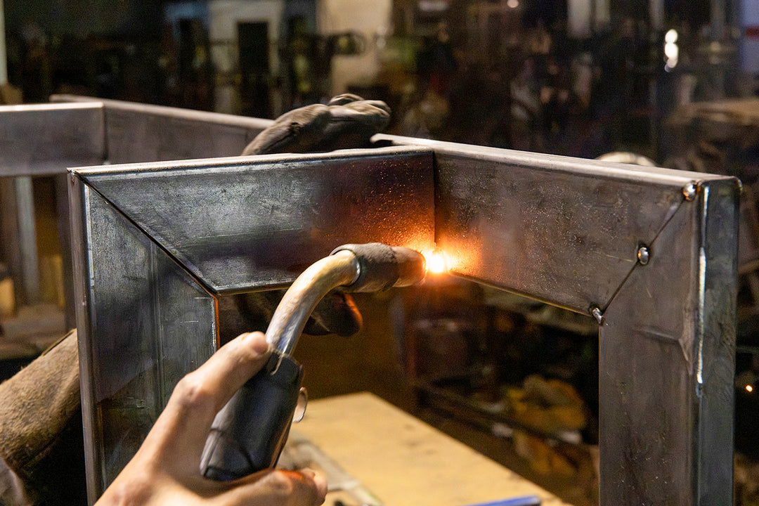 Skilled artisan assembling and joining shaped iron components to form the structural framework of a made-to-order lighting fixture.
