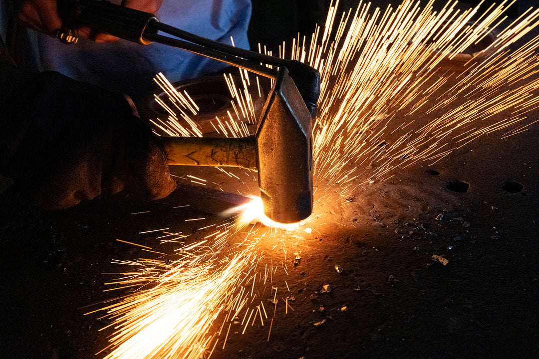 Artisan shaping iron by hand in the Ashore Lighting workshop as sparks fly during the fabrication of a made-to-order fixture.