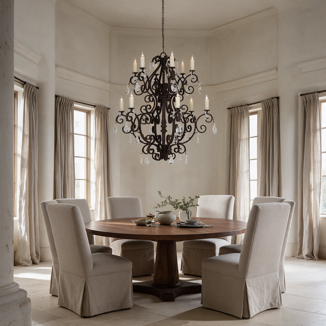 Monte Carlo Heritage wrought iron crystal chandelier above a round walnut dining table in a formal room with tall windows and linen chairs.