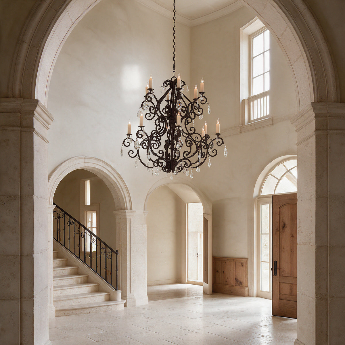 Monte Carlo Heritage 12-light wrought iron crystal chandelier hanging in a limestone foyer with tall arches and a sweeping staircase.