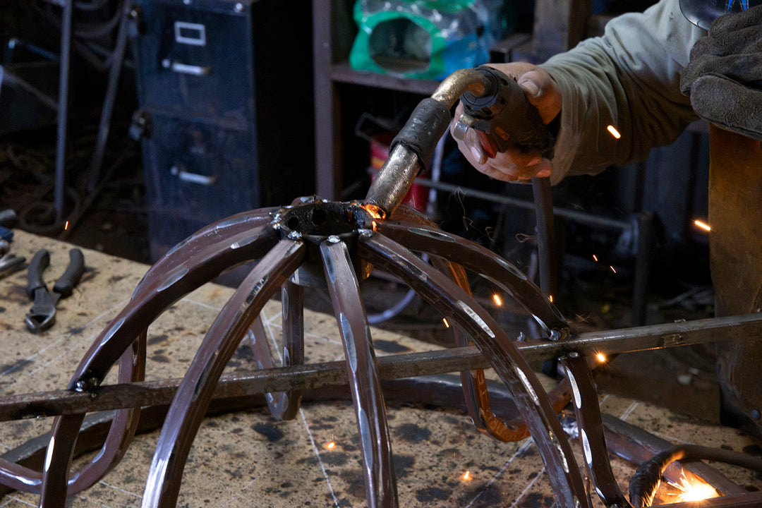 Ashore Lighting artisan welding curved iron components during the in-house construction of a made-to-order chandelier frame.